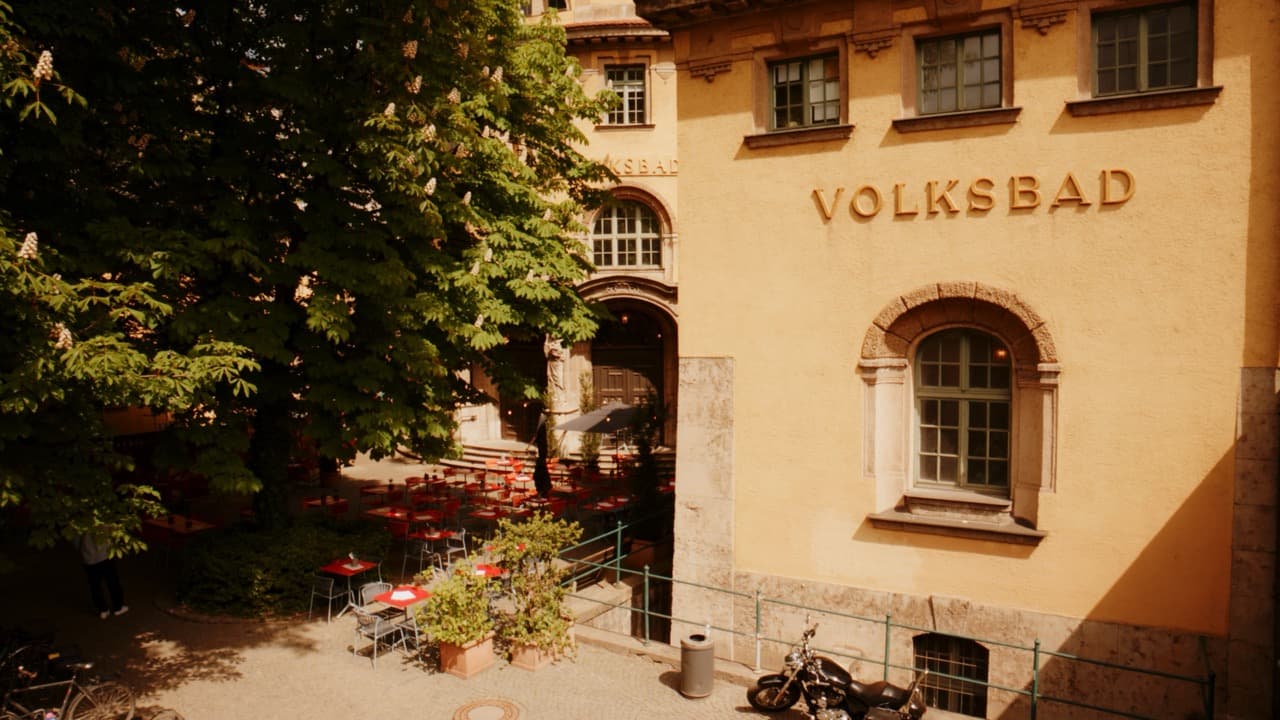 Sonnige Terrasse mit roten Stühlen vor der Volksbad-Fassade
